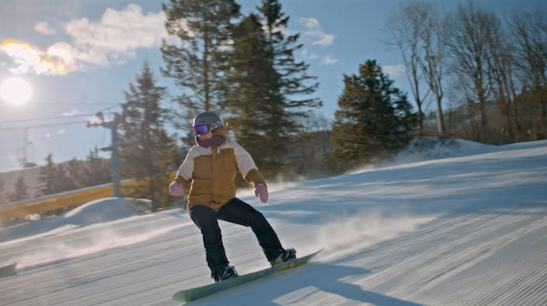 A snowboarder carves down a sunlit groomed run at Camelback Resort, spray lifting behind the board.